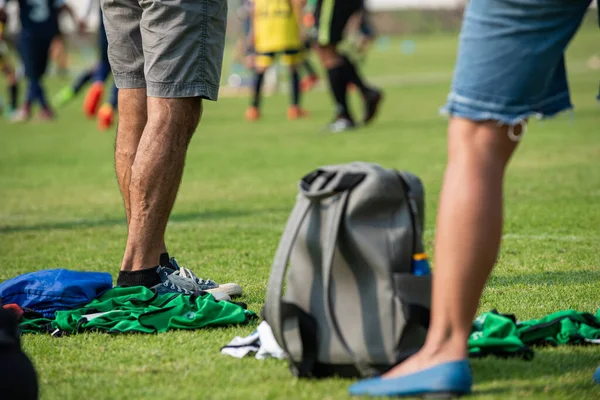 Anne ve baba açık havada ve güneşli bir günde oğullarının okul turnuvasında futbol oynamasını seyrediyor. Spor, aktif yaşam tarzı, mutlu aile ve ev hanımı, futbolcu baba kavramı.