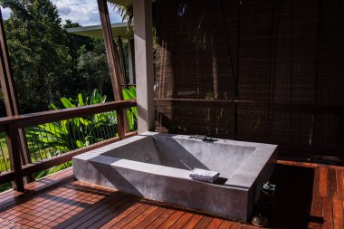 Gri granit açık hava jakuzisi ve spa havuzu. Kahverengi ahşap teras ve Tayland 'da lüks bir tepe oteli için güzel bir tropikal manzara tasarımı ile çevrili..
