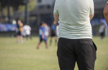 Baba, oğlunun güneşli bir günde bir okul turnuvasındaki futbol maçını seyrediyor. Spor, açık hava etkinliği, yaşam tarzı, mutlu aile ve futbol annesi ve futbolcu baba kavramı..