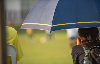 Ebeveynler açık havada ve güneşli bir günde okul turnuvasında oturup oğullarının futbol oynamasını izliyorlar. Spor, açık hava aktiviteleri, yaşam tarzı ve mutlu bir aile. Futbol anne ve baba kavramı.