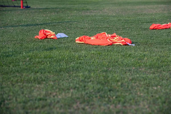 Colourful bibs left on a football pitch, ready for the next training session to come while footballers are drilling on the pitch with a coach with a clear sky in summer time.