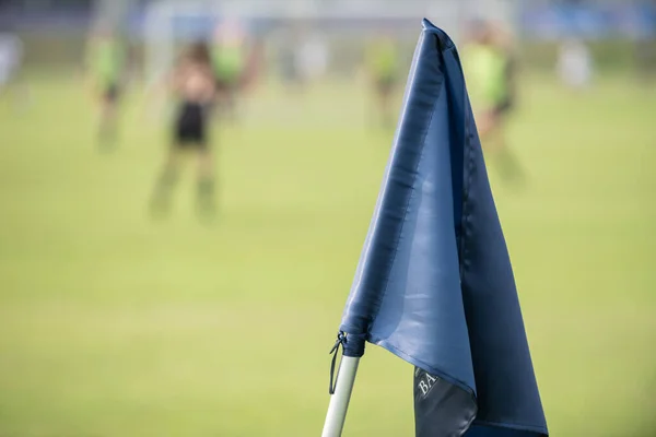 Blue corner flag from a football pitch, seeing group of players getting together as a team in a background. Atmosphere from a youth football tournament in a summer time.