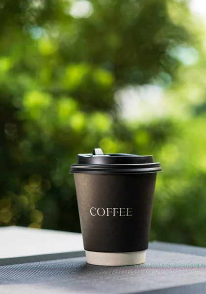 Coffee break with a take away paper cup full of hot coffee placed on a grey plastic placemat. Sunlight in the morning shines with a Mountain view as a background. Relax and warm feeling.