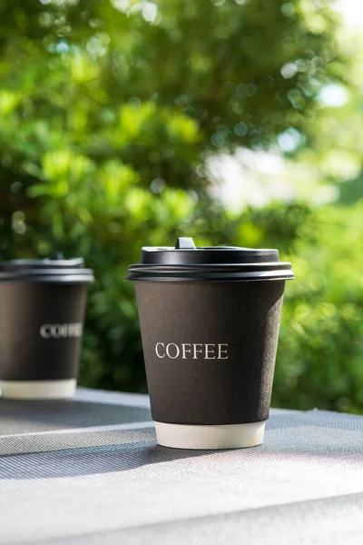 Coffee break with take away paper cups full of hot coffee placed on grey plastic placemats. Sunlight in the morning shines with a Mountain view as a background. Relax and warm feeling.