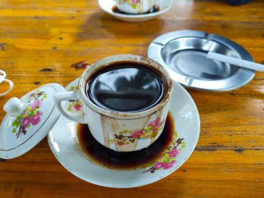 Kül tablası ve sigara ile ahşap zemin üzerinde beyaz bir fincan balck kahve