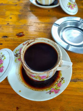 Kül tablası ve sigara ile ahşap zemin üzerinde beyaz bir fincan balck kahve