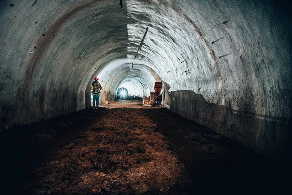 Siyah elbiseli bir adam büyük bir sırt çantasıyla taş bir duvarın arkasında.