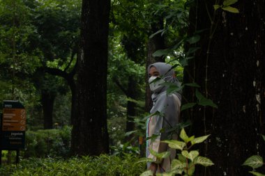 Parktaki ağacın arkasındaki kadın.