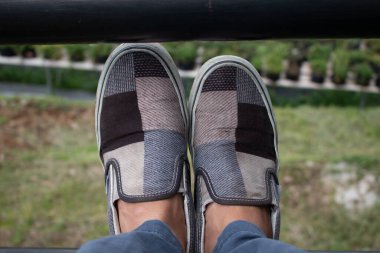 Bir çift sıradan ayakkabı, ekose, yeşil bir bitki arka planında duruyor.