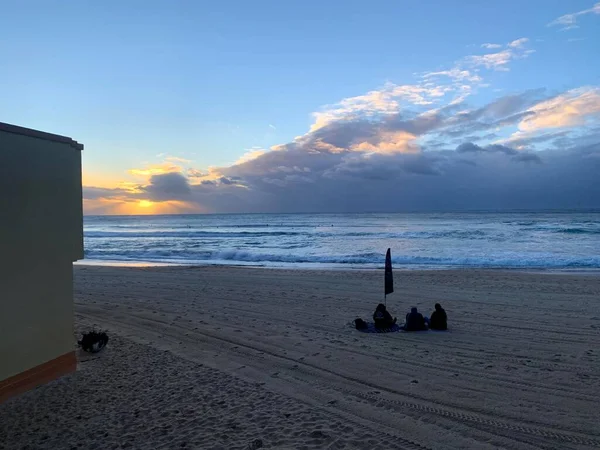 Kumsalda fırtınalı gün doğumu, meditasyon yapan insanlar.