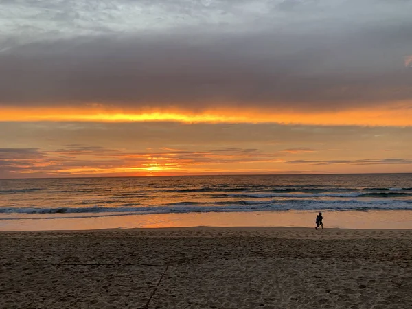 Sahilde yürüyen aylaklarla dalgaların üzerinde altın gün doğumu