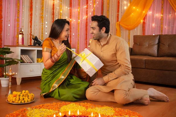 Young Indian couple - Happy husband gifting his wife on Diwali festival. Indian festival Diwali celebration at home - happy family, hindu festival, rangoli at home, colorful festival decoration, gift