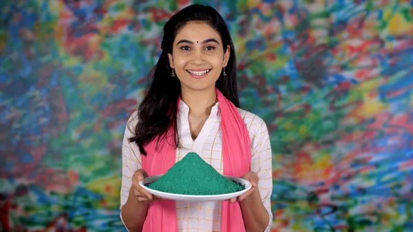 A beautiful Indian lady with a plate of vibrant Gulal (green) on the Holi festival  - leisure time, Indian culture and traditions. A youngster wearing a printed white Kurti and a Dupatta happily .....