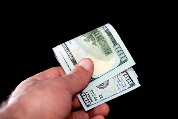 man's hand holds a stack of folded American currency of 100 $ one hundred American dollar bills, spending, giving, pay, buy and using money banknote concept  isolated on black background
