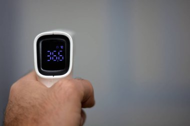 Vücut ısısını ölçtükten sonra sol elle tıbbi personelin tuttuğu temassız kızıl ötesi alın dijital termometresi. Yakın görünüm