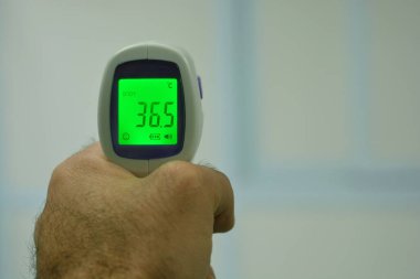 Vücut ısısını ölçtükten sonra sol elle tıbbi personelin tuttuğu temassız kızıl ötesi alın dijital termometresi. Yakın görünüm