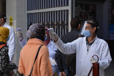 Bina girişinden önce katı önlemler, yüz maskeleri, el jelleri, temassız kızılötesi termometre ile sıcaklık taraması ve koronavirüs küresel kriz salgınının ortasında covid-19 yayılmasını önlemeye çalışan sosyal mesafeler