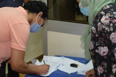 Koronavirüs aşısı olmadan önce Coronavirus aşısı belgelerini imzalayan öğrenciler, Mısır üniversiteleri aşı öğrencileri, yeni öğretim yılı öncesinde çalışanlar, aşı olmadan önce koronavirüs aşısı onayını okuyup imzalıyorlar.