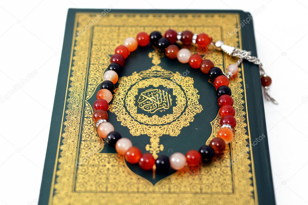 The holy Quran, Qur'an or Koran (the recitation) is the central religious text of Islam, believed by Muslims to be a revelation from God (Allah), isolated on white background with a rosary on it