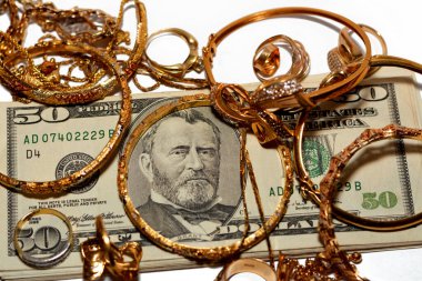 Bir yığın Amerikan doları para banknotları bir dizi altın aksesuar yüzük, kolye zinciri ve bilezikler beyaz arka planda izole edilmiş, altın değer, sat ve satın al konsepti, seçici odaklanma