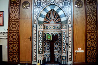 İçeriden bir cami, İslami dekoratif stile sahip, Mihrab camii veya Kur 'an' ı ahşap bir standa ve mikrofona yerleştirilmiş, Arapça çevirisi (Allah en büyüktür), seçici odaklı.