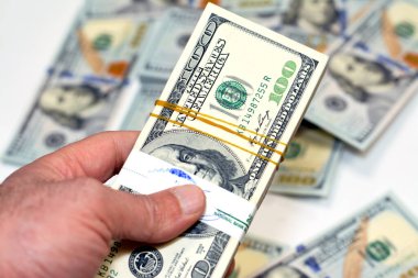 100 Amerikan dolarının destesini tutan adam para, harcama, para verme ve kullanma kavramını kullanarak, 100 Amerikan dolarının bulanık arka planındaki banknotları kullanarak ve satın alarak