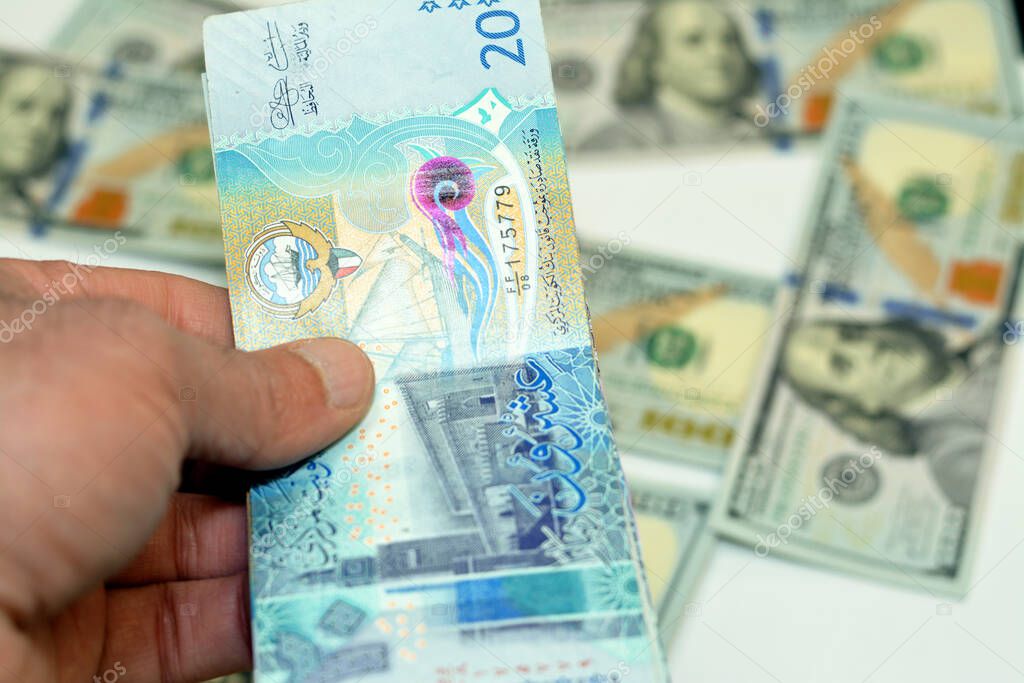 man hand holding a stack of 20 twenty Kuwaiti dinars banknotes money, spending, giving and using money concept, paying and buying using banknotes on blurred 100 American dollars background