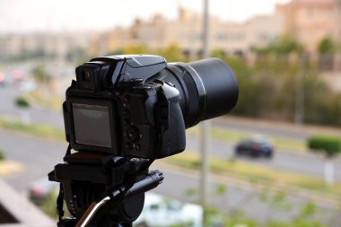 Zaman atlaması için tripoda sabitlenmiş bir dijital kamera ve şehrin caddelerini ve binalarını bulanık bir şekilde gösteren video kaydı, güneşi, gökyüzünü ve bulutları çeken ufuk çizgisini gösteriyor.