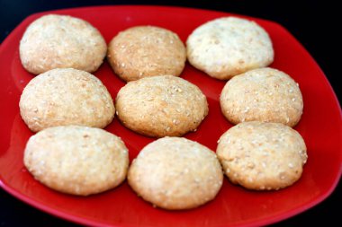 Arap Mısırlı, içi hurma dolu kurabiyeler ve susamlı, Maamoul Kurban Bayramı ziyafeti, Ramazan tatlısı ve tatlılar ile kaplanmış siyah arka planda izole edilmiş kırmızı bir tabak, seçici bir odak