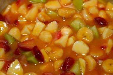 Dilimlenmiş muz, çilek, kavun, elma, mango ve portakal suyu karışımından yapılmış meyve salatasının yakın çekimi, vitamin ve minerallerle dolu taze dilimlenmiş meyvelerin seçici odağı