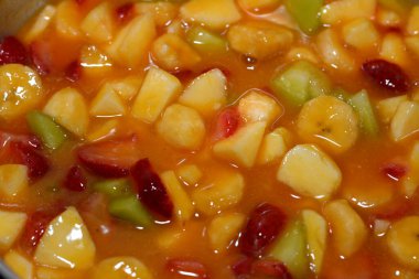 Dilimlenmiş muz, çilek, kavun, elma, mango ve portakal suyu karışımından yapılmış meyve salatasının yakın çekimi, vitamin ve minerallerle dolu taze dilimlenmiş meyvelerin seçici odağı