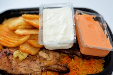 Arabic Syrian cuisine of charcoal grilled barbecued chicken with colorful Basmati rice and fried chips potatoes served in a black disposable plate usually served with regular and spicy garlic sauce