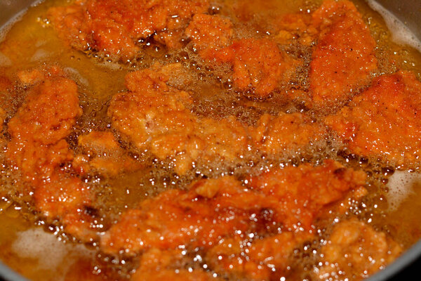 Frying chicken strips in deep oil background, selective focus of chicken fingers, tenders, fillet or goujons are white chicken meat from either sides of breast bone