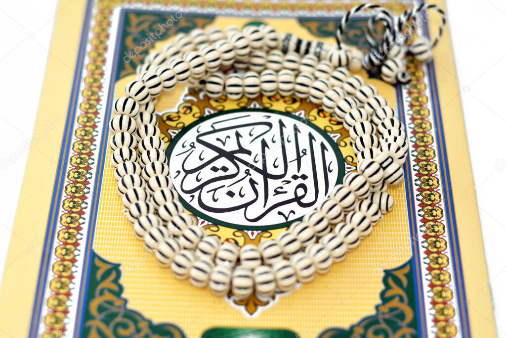The holy Quran, Qur'an or Koran (the recitation) is the central religious text of Islam, believed by Muslims to be a revelation from God (Allah), isolated on white background with a rosary on it