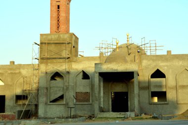 Caminin minaresi ve kubbeleri ahşap iskeleler ve inşaat halindeki pencerelerle çevrili güneşli mavi gökyüzüne karşı inşa halindeki yeni bir cami, cami dışarıdan henüz bir çimento.