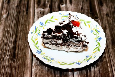 Kara Orman pastasından dilimlenmiş bir parça, kiraz şurubu ve kiraz brendisiyle ıslatılmış hafif çikolatalı bir kek (Kirsch), sonra da ahşap bir arka planda izole edilmiş krema ve kirazlarla kaplanmış.