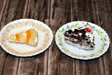 Dilimlenmiş bir parça kara orman pastası, çırpılmış krema ve kiraz katmanlı çikolatalı kek ve ahşap bir zeminde taze meyveli bir dilim tropikal meyveli kek.