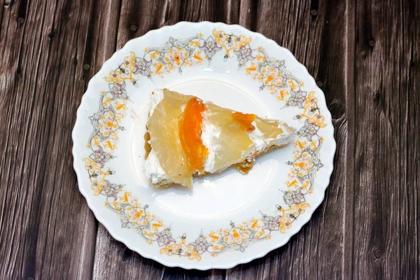 A slice of tropical fruit tart cake with fresh pieces of apple, slices of fresh beach and pineapples layered with whipped cream based on a simple shortbread crust isolated on wooden background