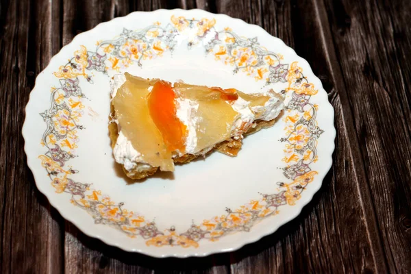 A slice of tropical fruit tart cake with fresh pieces of apple, slices of fresh beach and pineapples layered with whipped cream based on a simple shortbread crust isolated on wooden background