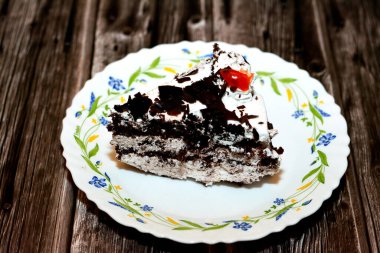 Kara Orman pastasından dilimlenmiş bir parça, kiraz şurubu ve kiraz brendisiyle ıslatılmış hafif çikolatalı bir kek (Kirsch), sonra da ahşap bir arka planda izole edilmiş krema ve kirazlarla kaplanmış.