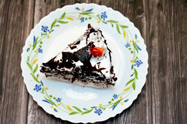 Kara Orman pastasından dilimlenmiş bir parça, kiraz şurubu ve kiraz brendisiyle ıslatılmış hafif çikolatalı bir kek (Kirsch), sonra da ahşap bir arka planda izole edilmiş krema ve kirazlarla kaplanmış.