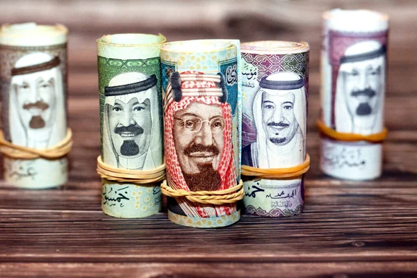 Saudi Arabia money roll riyals banknotes isolated on wooden background, Saudi riyals cash money bills rolled up with rubber bands of 100 SAR, 50, 20, 10 and 5 riyal, selective focus