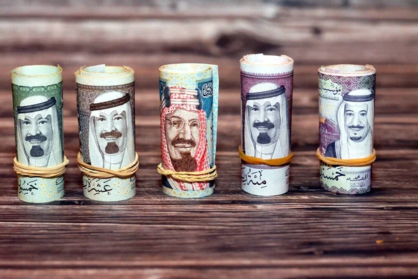 Saudi Arabia money roll riyals banknotes isolated on wooden background, Saudi riyals cash money bills rolled up with rubber bands of 100 SAR, 50, 20, 10 and 5 riyal, selective focus