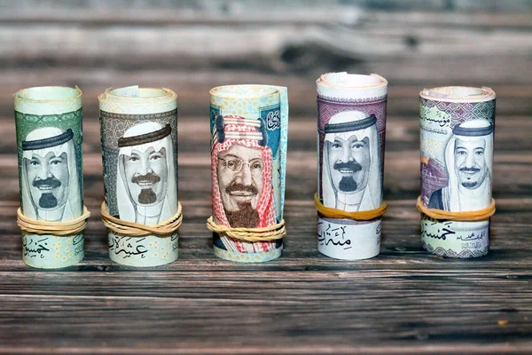 Saudi Arabia money roll riyals banknotes isolated on wooden background, Saudi riyals cash money bills rolled up with rubber bands of 100 SAR, 50, 20, 10 and 5 riyal, selective focus