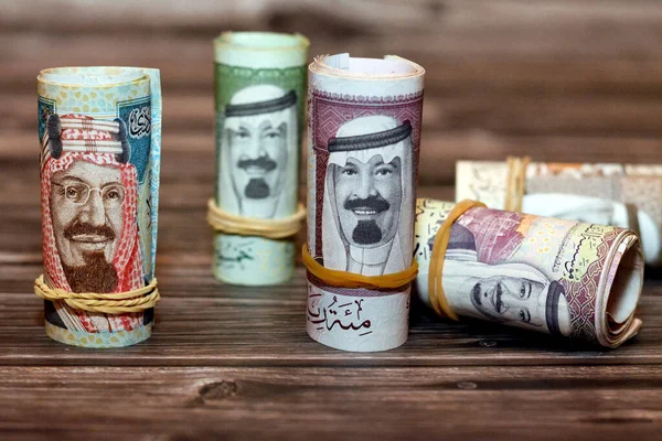 Saudi Arabia money roll riyals banknotes isolated on wooden background, Saudi riyals cash money bills rolled up with rubber bands of 100 SAR, 50, 20, 10 and 5 riyal, selective focus
