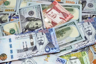 Pile of 100 $ one hundred dollar bills American cash money banknotes with Saudi Arabia riyals money banknotes of 500 riyals, 100 and 50 riyal, American and Saudi money exchange rate, selective focus