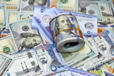 American money roll with a band on a pile of American dollar bills American cash money banknotes with Saudi Arabia riyals money banknotes and New Emirates polymer dirhams, Cash money exchange rates