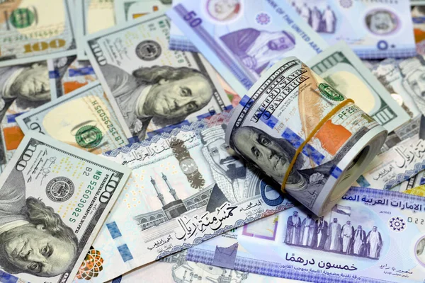 American money roll with a band on a pile of American dollar bills American cash money banknotes with Saudi Arabia riyals money banknotes and New Emirates polymer dirhams, Cash money exchange rates