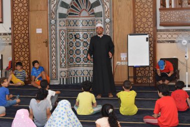 Cairo, Egypt, August 7 2022: A mosque preacher Imam performs a religious Khutbah (sermon) for young Muslim children inside a mosque during the summer Islamic educational program for kids in the mosque