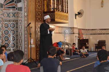 Cairo, Egypt, August 7 2022: A mosque preacher Imam performs a religious Khutbah (sermon) for young Muslim children inside a mosque during the summer Islamic educational program for kids in the mosque